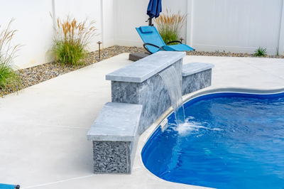 Three-tiered natural stone waterfall cascading into a backyard pool with surrounding ornamental grasses