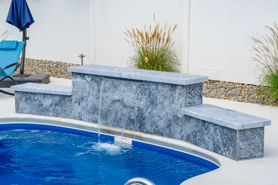 Three-tiered natural stone waterfall sheeting into a backyard pool bordered by ornamental grasses