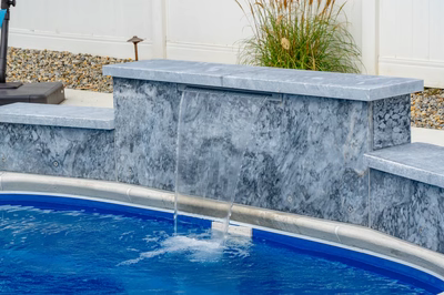 Multi-tiered natural stone boulder waterfall with sheet flow cascading into a pool near grass