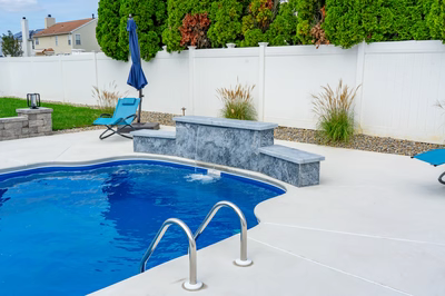 Three-tiered natural stone waterfall cascading into a backyard pool bordered by lush ornamental grasses