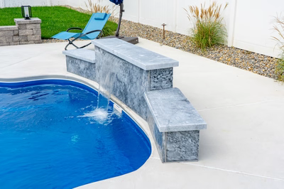 Three-tiered natural stone boulder sheet waterfall cascading into a pool with surrounding garden plants