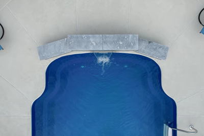 Single-tier natural stone boulder waterfall with sheer descent flow cascading into a vibrant blue pool