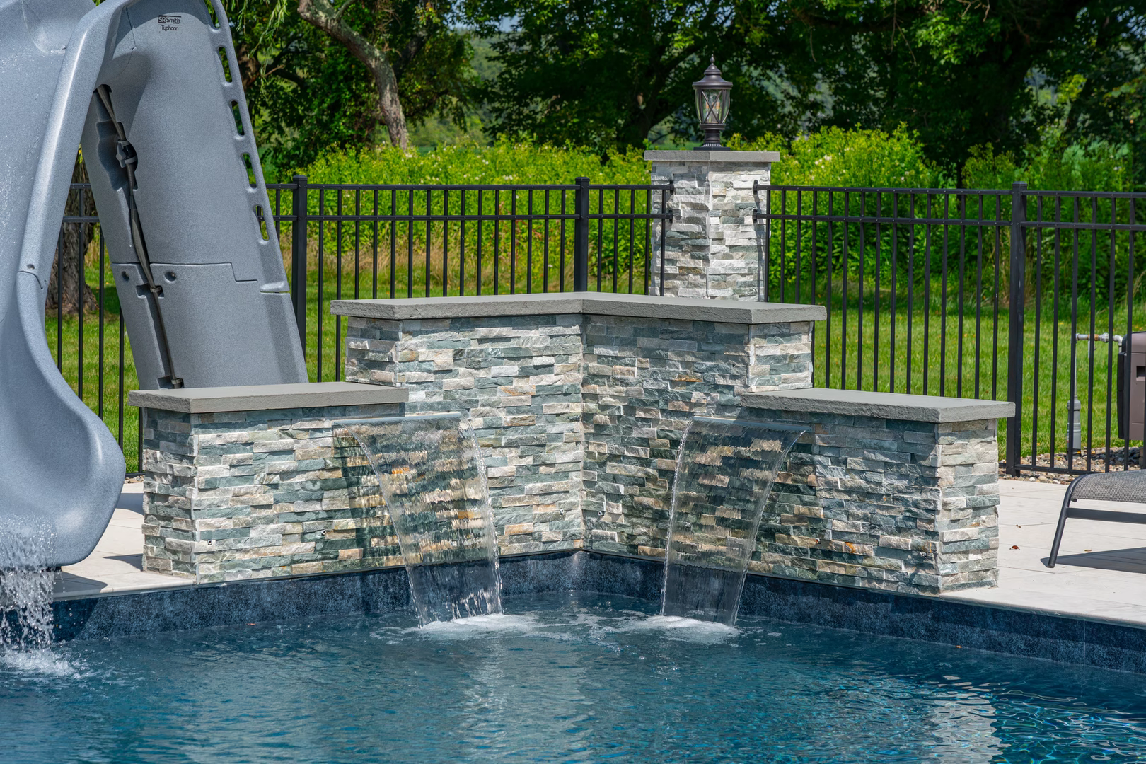 Natural stone boulder waterfalls cascade into a pool bordered by lush green foliage