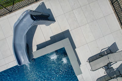 Modern single-tier grey waterfall feature spilling into a blue pool with large format pavers