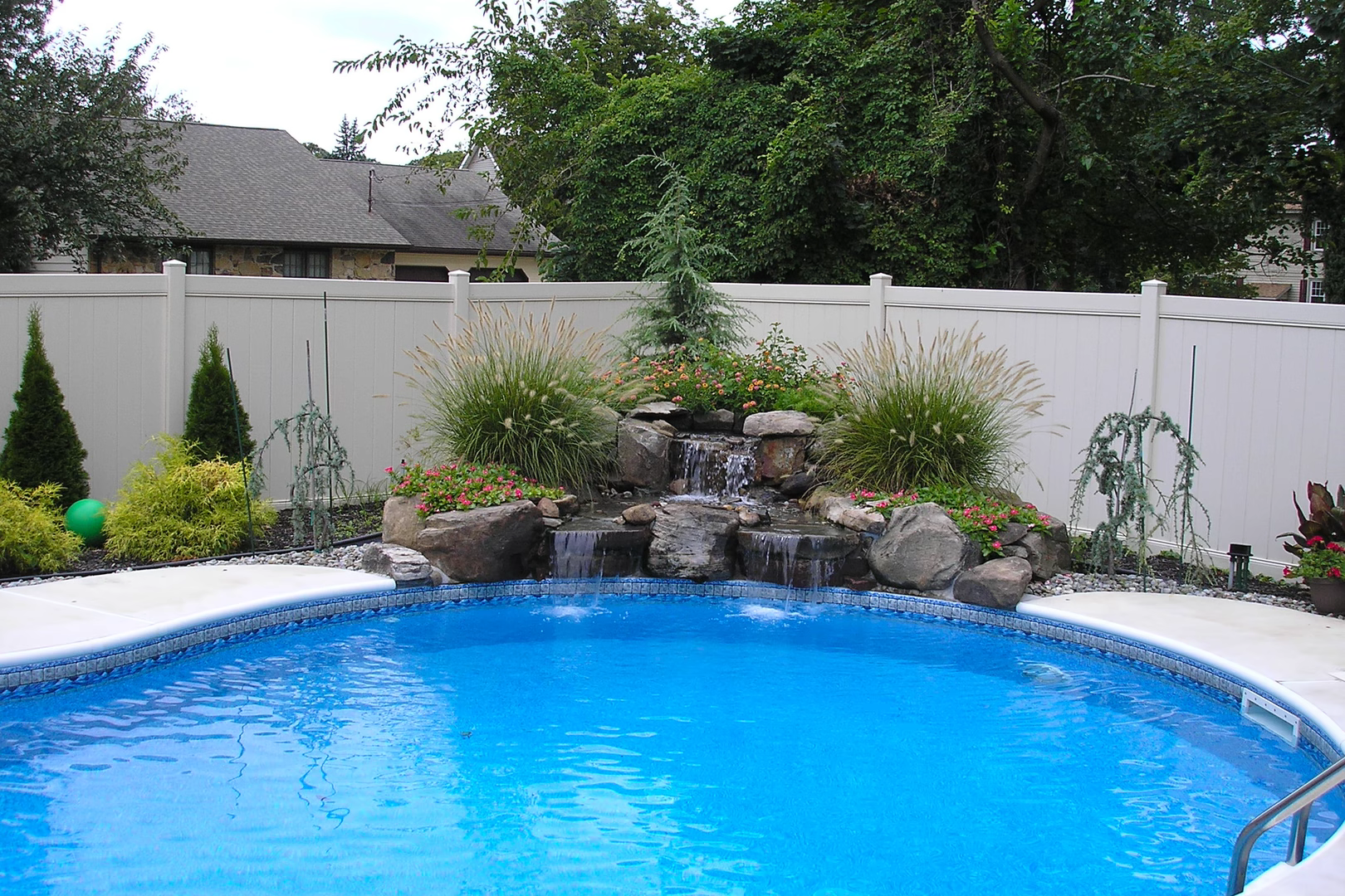 Natural stone boulder waterfall cascading into a pool surrounded by ornamental grasses and evergreens