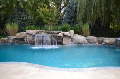 Single-tier natural stone boulder waterfall cascading into a pool surrounded by lush garden greenery