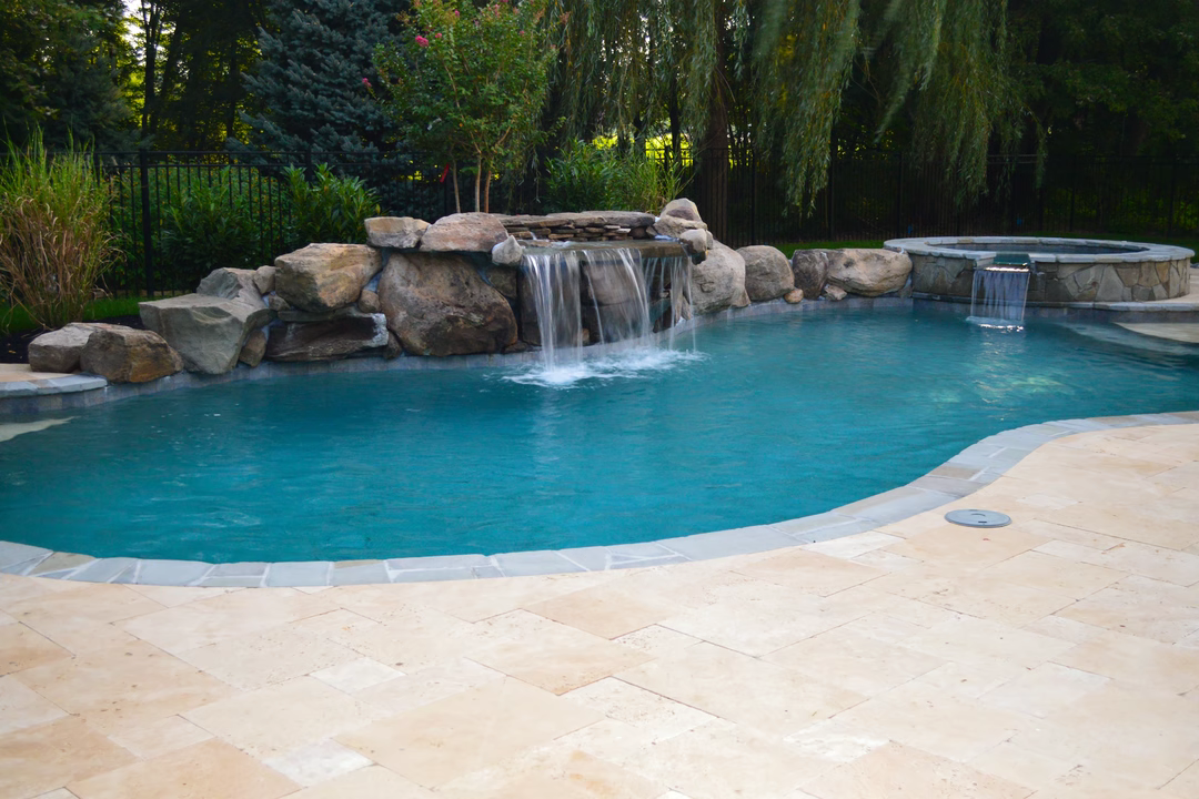 Multi-tiered natural stone boulder waterfall cascading into a freeform pool surrounded by lush greenery