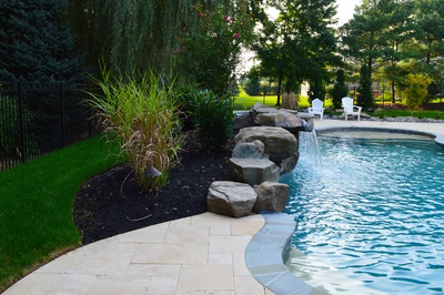 Multi-tiered natural stone boulder waterfall cascading into a clear pool surrounded by lush landscaping