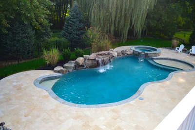 Double-tiered natural stone boulder waterfall cascading into a freeform pool surrounded by lush greenery