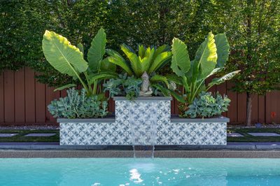 Three-tiered geometric tiled waterfall spilling into a pool surrounded by lush tropical greenery