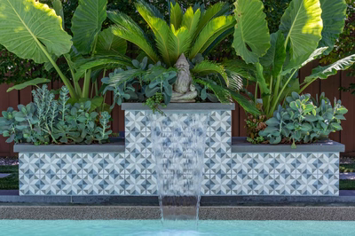 Three-tiered tiled sheer descent waterfall spilling into a pool framed by lush tropical foliage