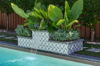 Two-tiered geometric tiled waterfall cascading into a pool surrounded by lush tropical plants