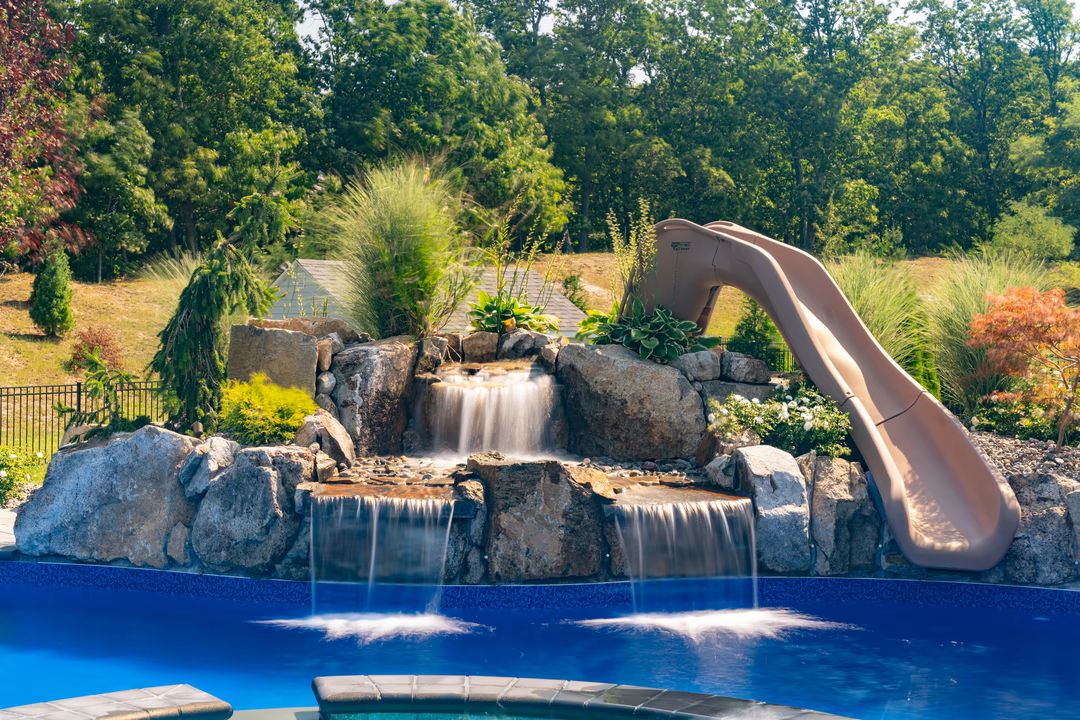 Multi-tiered natural stone boulder waterfalls cascading into a blue pool surrounded by lush greenery