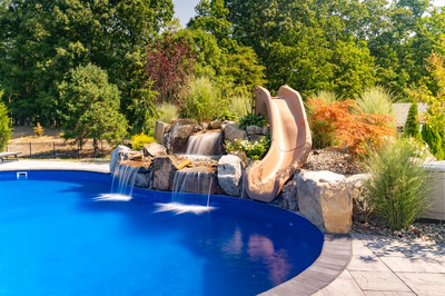 Triple-tiered natural stone boulder waterfall cascading into a blue pool with lush landscaping