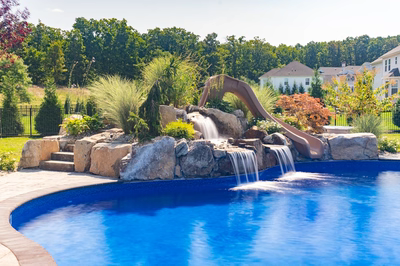 Multi-tiered natural stone boulder waterfall cascading into a blue pool with lush ornamental landscaping