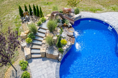 Two-tiered natural stone waterfall cascading into a blue pool surrounded by lush ornamental landscaping