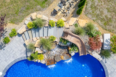Multi-tiered natural stone boulder waterfall cascading into a pool surrounded by lush garden plants