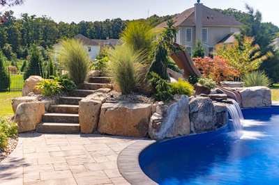 Single-tier natural stone boulder waterfall cascading into a pool surrounded by lush ornamental garden plants