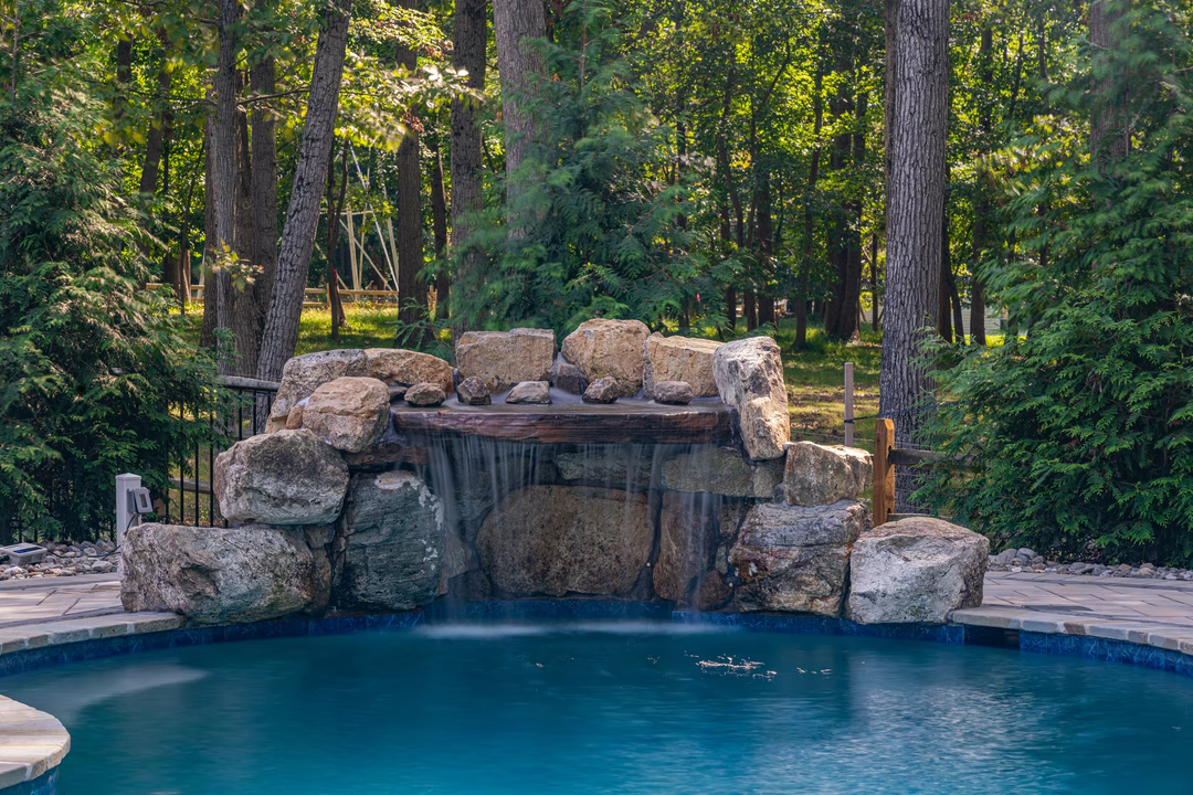 Single-tier natural stone boulder waterfall cascading into a pool surrounded by lush green trees