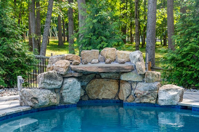 Two-tiered natural stone boulder waterfall cascading into a pool surrounded by dense green forest