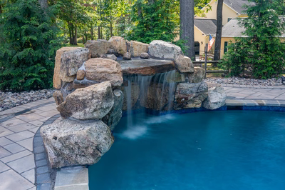 Single-tier natural stone boulder waterfall cascading into a pool surrounded by lush green trees
