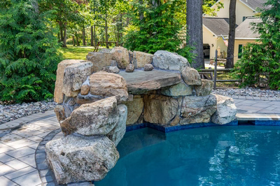 Multi-tiered natural stone boulder waterfall cascading into a pool surrounded by lush green trees