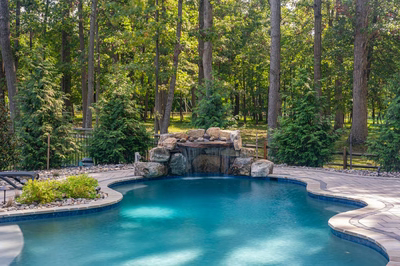 Single-tiered natural stone boulder waterfall with sheet flow into a freeform pool beside evergreen trees