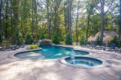 Two-tiered natural stone boulder waterfall cascading into a freeform pool surrounded by lush greenery