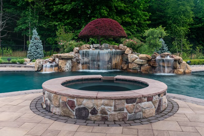 Multi-tiered natural stone boulder waterfalls cascading into a pool with lush garden landscaping
