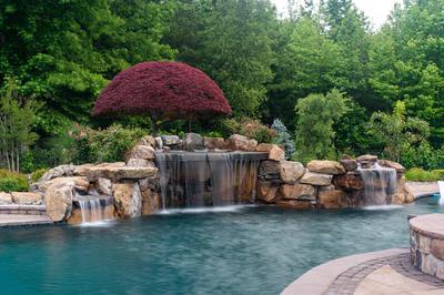 Multi-tiered natural stone boulder waterfalls cascade into a pool surrounded by lush, vibrant landscaping