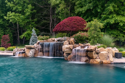 Multi-tiered natural stone boulder waterfalls cascade into a pool surrounded by lush garden landscaping