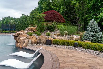 Natural stone boulder waterfall cascading into a pool surrounded by lush garden landscaping