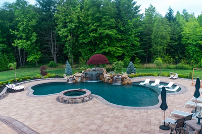 Triple-tiered natural stone boulder waterfall cascading into a freeform pool with lush forest surroundings