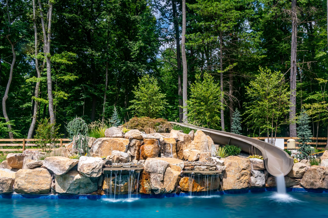 Three-tiered natural stone boulder waterfall cascading into a pool surrounded by lush forest greenery