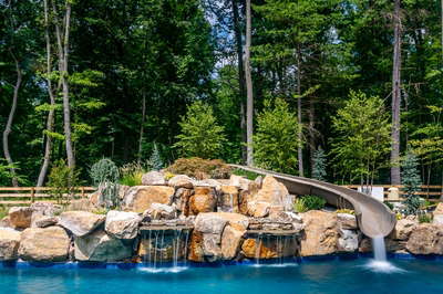 Three-tiered natural stone boulder waterfall cascading into a pool surrounded by lush forest greenery