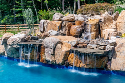 Multi-tiered natural stone boulder waterfalls cascading into a blue pool surrounded by lush greenery