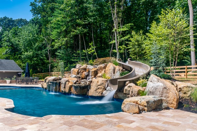 Multi-tiered natural stone boulder waterfall cascading into a pool surrounded by lush forest greenery