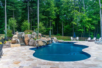 Multi-tiered natural stone boulder waterfall cascading into a freeform pool surrounded by lush forest
