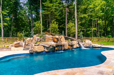 Multi-tiered natural stone boulder waterfall cascading into a freeform pool surrounded by lush greenery