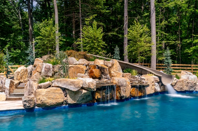 Triple-tiered natural stone boulder waterfall cascading into a pool surrounded by lush forest trees