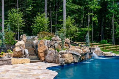 Multi-tiered natural stone boulder waterfall cascading into a pool surrounded by lush forest greenery