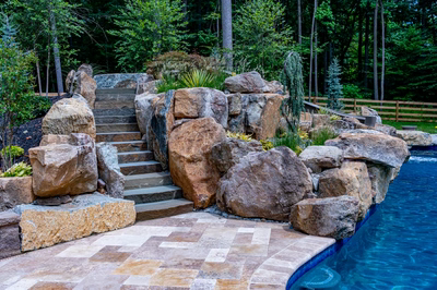 Multi-tiered natural stone boulder waterfall cascading into a pool surrounded by lush forest plants