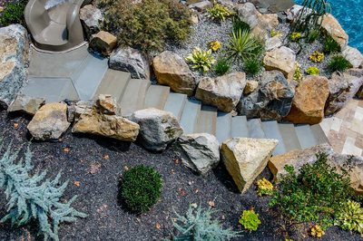 Multi-tiered natural stone boulder waterfall cascading into a pool surrounded by vibrant garden plants