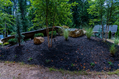 Multi-tiered natural stone boulder waterfall cascading into a pool surrounded by lush garden plants