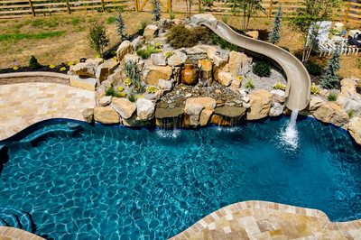 Multi-tiered natural stone boulder waterfalls cascading into a freeform pool with lush greenery
