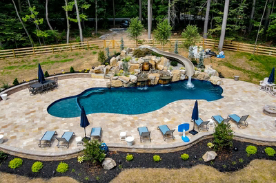 Multi-tiered natural stone boulder waterfall cascades into a freeform pool surrounded by lush landscaping