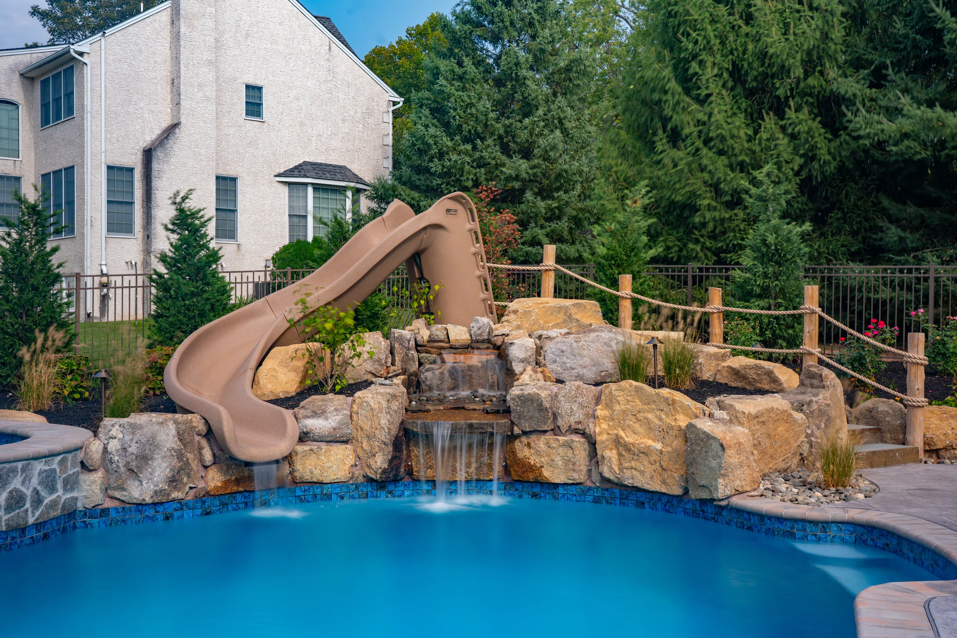 Two-tiered natural stone boulder waterfall cascading into a pool surrounded by lush garden plants