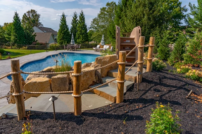 Multi-tiered natural stone boulder waterfall cascading into a freeform pool with lush garden plants