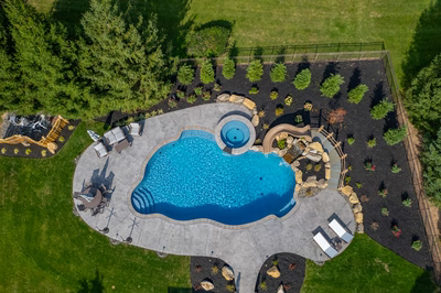 Multi-tiered natural stone boulder waterfall cascading into a backyard pool near tall evergreen trees