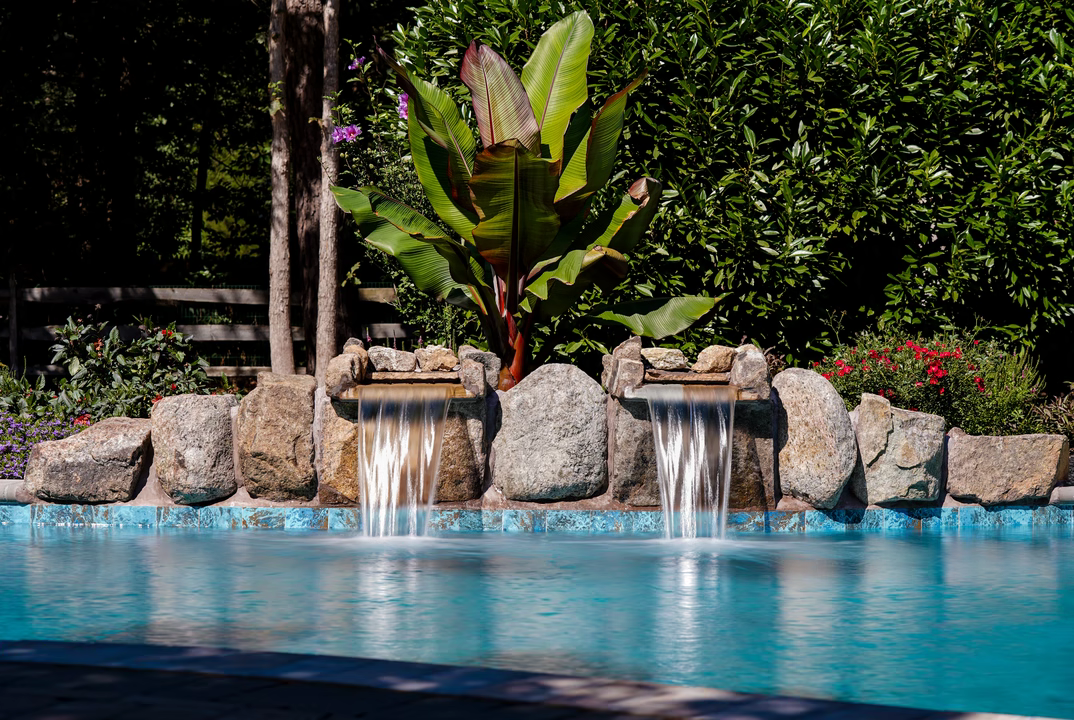Twin single-tier natural stone boulder waterfalls cascading into a pool with lush tropical landscaping